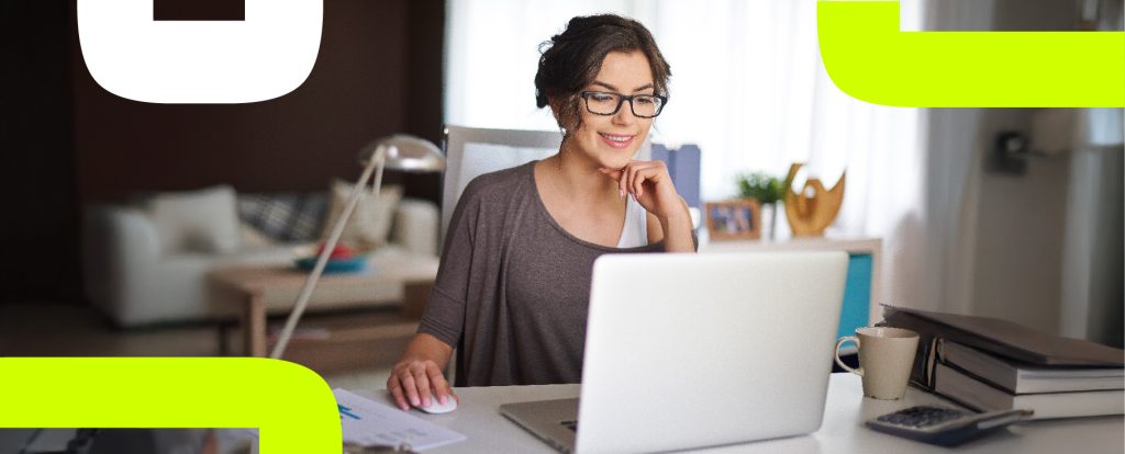 Mulher sorridente usando óculos e blusa cinza trabalha em um laptop em um ambiente acolhedor de home office, com uma mesa organizada contendo uma caneca, pilha de documentos e calculadora. Ao fundo, uma sala de estar com sofás e objetos decorativos. Elementos gráficos em verde neon enquadram a imagem.